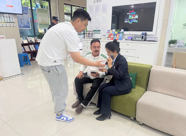 图为：邮储银行黔东南州分行营业部业务人员借助中英文转换APP与外籍客户交流.png