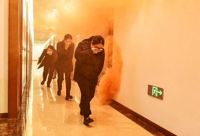 1769676877579398.jpg 图为:演练模拟办公区起火,火势蔓延并产生浓烟,参训人员低姿弯腰、湿毛巾捂口鼻,沿预定通道快速撤离2.jpg