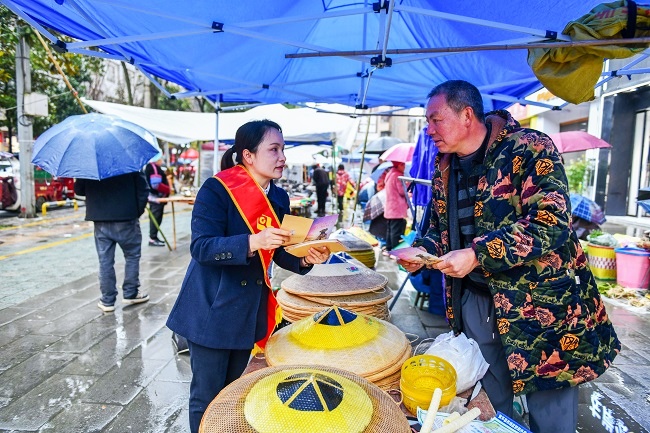 图为：工作人员冒雨走进集市摊位，向摆摊商户讲解金融知识，守护百姓“钱袋子”.jpg