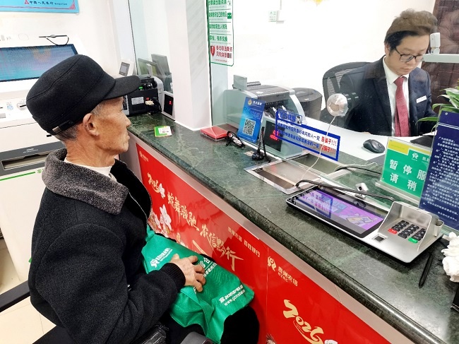 1774938820582281.jpg 图为:杨大叔手持珍藏多年的绿布袋在柜台前办理业务.jpg